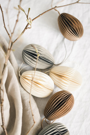 Easter egg-shaped pastel colored decorations, made out of cardboard and branches on linen tablecloth.の写真素材