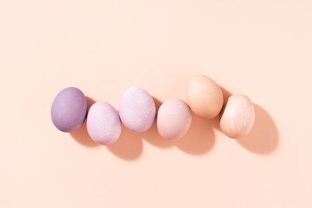 Row of pastel colored Easter eggs on peach background, top view, hard light.の写真素材