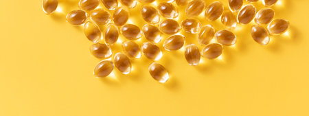 Banner with closeup of oil gel capsules on yellow background. Suitable for: Omega 3, Vitamin D, Vitamin E, Omega 6, or Omega 9.の写真素材
