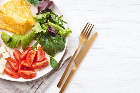French omelet, avocado, tomatoes, salad, and cheese on plate. Healthy breakfast on white table, top view.の写真素材