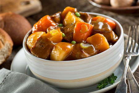 A delicious bowl of rich and hearty beef stew with potato, turnip, carrot, celery, and peas.の写真素材
