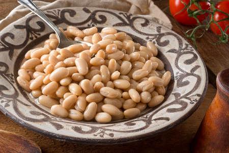 A bowl of white kidney beans on a rustic wooden table top.の写真素材