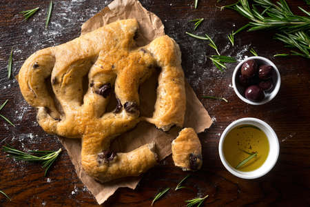 A delicious focaccia bread with black olives and rosemary on a rustic tabletop.の写真素材