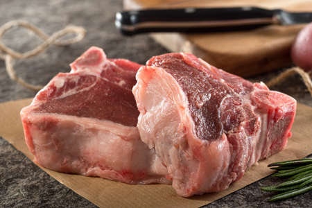 Two beautifully marbled raw lamb chops on paper with butchers twine and rosemary.