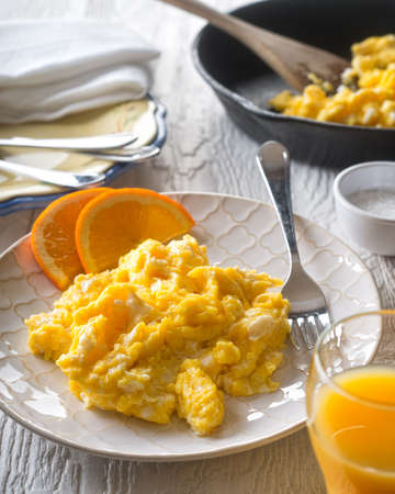 A plate of delicious fresh scrambled eggs with orange slices and orange juice.の写真素材