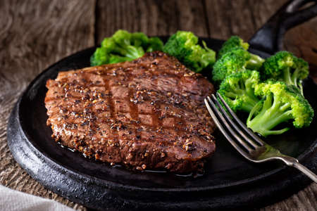 A delicious grilled pepper steak with broccoli on a rustic wooden table.の写真素材