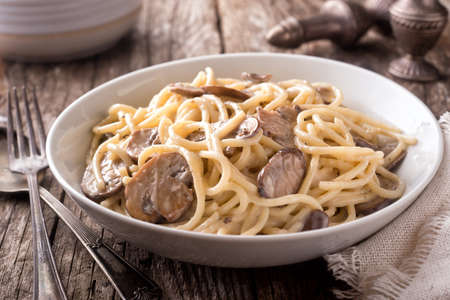 A bowl of delicious pasta alfredo with mushrooms on a rustic table top.の写真素材