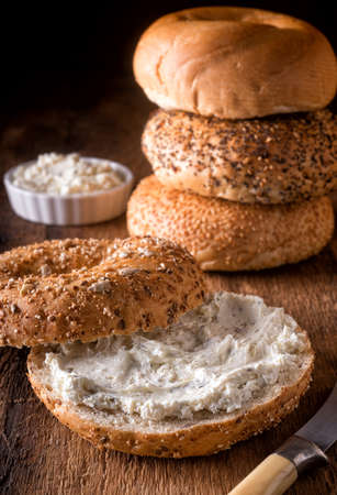 A delicious whole grain bagel with herbed cream cheese on a rustic wood table.の写真素材