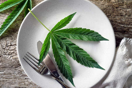 Conceptual image of a cannabis leaf on a plate with a knife and fork.の写真素材
