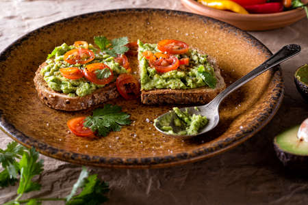 A slice of delicious avocado toast with sliced tomato and cilantro.