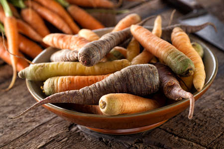 Raw fresh organic heirloom carrots in a bowl on a rustic harvest table.の写真素材
