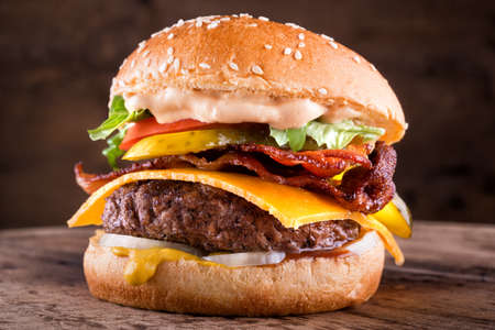 A delicious homemade bacon cheeseburger with real cheddar cheese, lettuce, onion, tomato, pickle, mustard, ketchup and burger sauce.の写真素材
