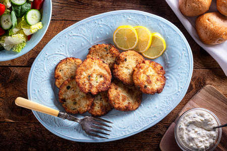 A platter of homemade fish cakes with tartar sauce, fresh rolls and garden salad.