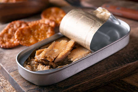 A can of smoked kippers and crackers on a rustic wood table top.