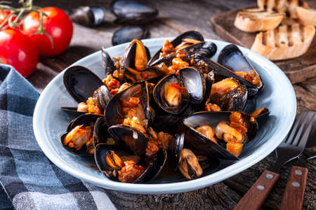 Delicious cajun style mussels jambalaya with sausage, celery, onion, pepper and tomato on a rustic table top.の写真素材