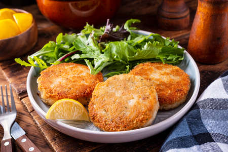 A plate of delicious fish cakes with spring mix salad and lemon garnish.の写真素材