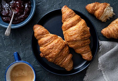 Delicious buttery croissants with jam and coffee on a blue background.