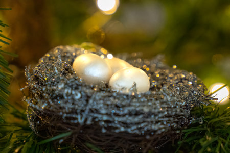 Eggs in a birds nest Christmas ornament in an artificial Christmas tree with Christmas light in backgroundの写真素材