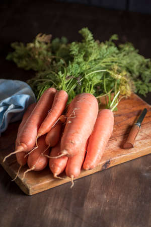 natural carrot on a wooden board next to a razor and a kitchen towel on dark backgroundの写真素材
