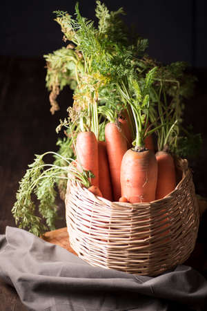 natural carrot inside a basket, on a wooden board, next to a razor and a dishcloth, on a dark backgroundの写真素材