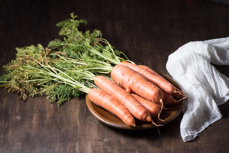 natural carrot on clay plate, on a wooden board, next to a razor and a dishcloth, on dark backgroundの写真素材