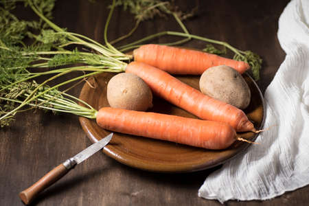 natural carrot on clay plate, on a wooden board, next to a razor and a dishcloth, on dark backgroundの写真素材