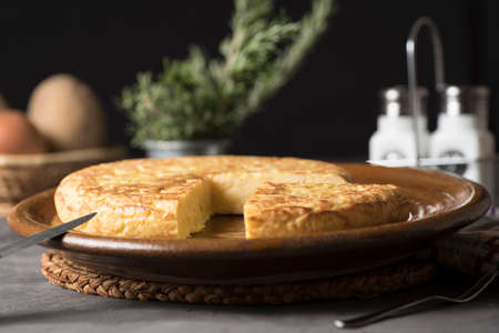 Spanish potato omelette, on a table, next to the necessary ingredients to be cooked and ready to be...