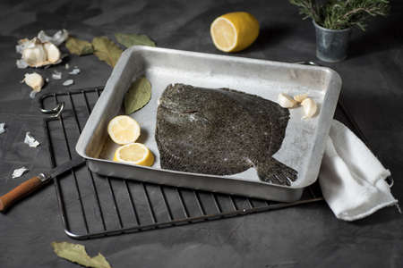 Turbot on a baking sheet and oven rack, with garlic, lemon and bay leaf, prepared to be baked in the...