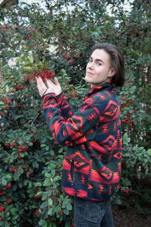young woman holding red berries from a mistrans bush while looking at camera