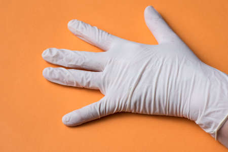 light colored sanitary glove, placed on one hand, on orange background
