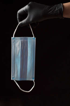 sanitary mask with one blue face and the other white with two elastic bands, held by one hand with a...