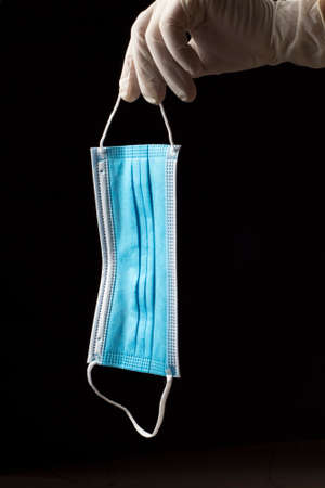 sanitary mask with one blue face and the other white with two elastic bands, held by one hand with a...