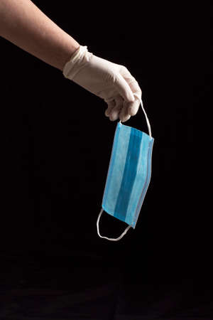 sanitary mask with one blue face and the other white with two elastic bands, held by one hand with a...