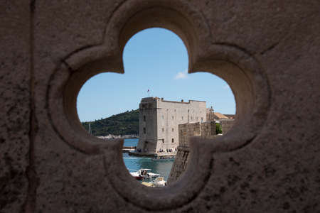 Views, through a cross-shaped hole located in a bridge, of the stone walls and the port in Dubrovnik, Croatia, Europe.のeditorial素材