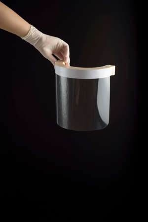 Hand with latex glove holding a face screen, on black background. Protection for contagions.の写真素材