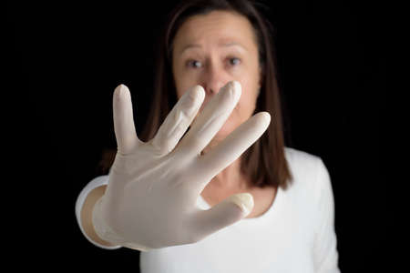 Forgive partially covering your face with one hand, with a latex glove, on a black background. Protection for contagions.の写真素材