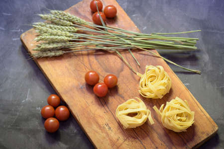 pasta nest of wheat flour, cherry tomatoes and ear of wheat on a wooden boardの写真素材