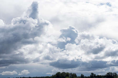Sky with lots of white and gray shaped clouds and very little ground spaceの写真素材