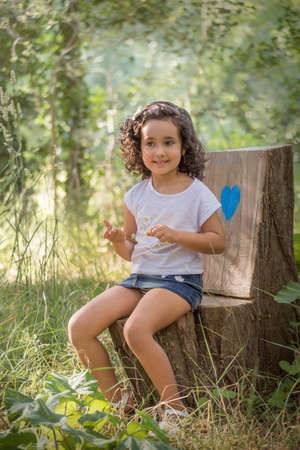 Girl in a white T-shirt and denim miniskirt sitting on a bench in a grove.の写真素材