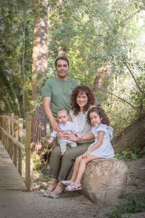 Family consisting of father mother baby and girl sitting on a log of wood in a grove.の写真素材