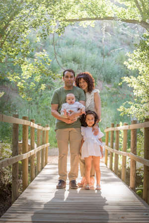 Family consisting of father mother baby and a girl posing on a wooden bridge in a grove.の写真素材