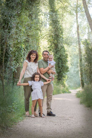 Family consisting of father mother baby and a girl posing in a grove surrounded by greenery.の写真素材
