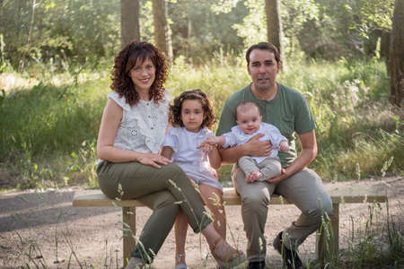 Family consisting of father mother baby and a girl sitting on a wooden toilet in a grove surrounded by greenery.の写真素材