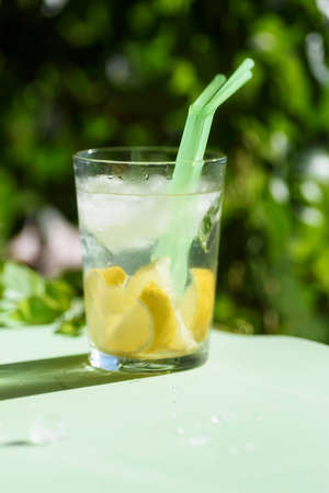 glass with refreshing drink with ice, lemon and straws, on a green background. Summer drink.の写真素材