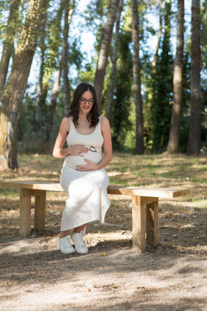 young pregnant woman sitting on a bench in the field.の写真素材