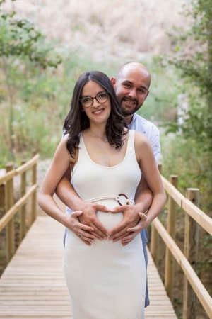 Cheerful Caucasian couple on maternity shoot in a wooden bridgeの写真素材