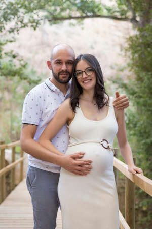 Cheerful Caucasian couple on maternity shoot in a wooden bridgeの写真素材