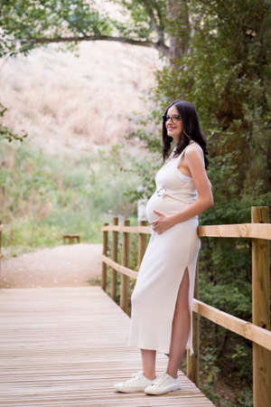 Cheerful Caucasian woman on maternity shoot in a wooden bridgeの写真素材