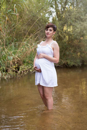 young pregnant woman sitting on a bench in the field.の写真素材