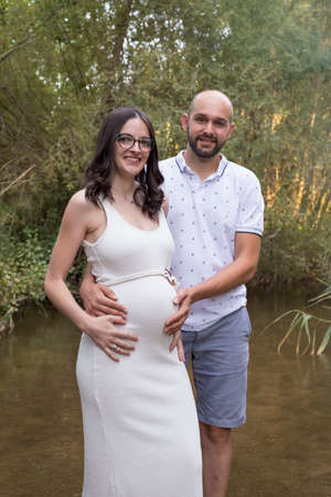 young pregnant woman, with her partner, sitting on a bench in the field.の写真素材